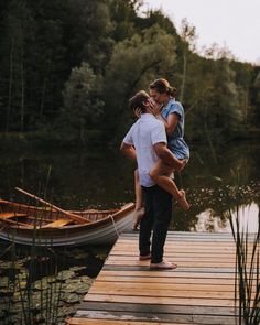 two people are standing on a dock with a boat in the water and one person is holding another