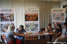 several people sitting around a table with posters on the wall behind them and one person writing