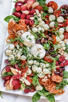 a white platter filled with salad and fruit on top of a marble countertop