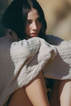 a woman sitting on the ground with her arms behind her head and looking off into the distance