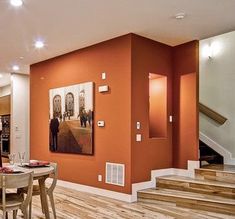 a dining room table and chairs in front of an orange wall with stairs leading up to it