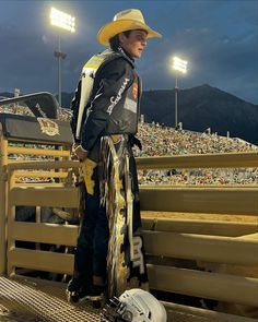 a man wearing a cowboy hat and scarf standing in front of a fence at a stadium