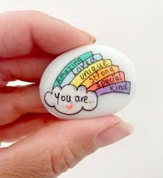 a hand holding a white button that says you are special kind with rainbows and clouds