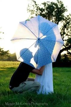 a man and woman kissing under an umbrella in the grass with trees in the background