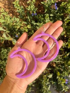 a pair of purple hoop earrings sitting on someone's hand in front of some bushes