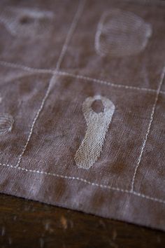 an embroidered piece of cloth with white stitching on it, sitting on top of a wooden table