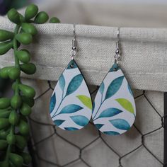 two pairs of earrings with blue and green leaves on them hanging from a wire fence