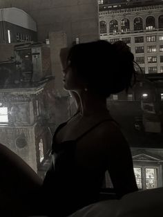 a woman standing in front of a window looking out at the city lights and buildings