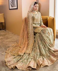 a woman sitting on top of a couch wearing a green and gold wedding dress with long veil