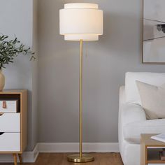 a living room with a white couch and a gold floor lamp in the middle of it