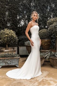 a woman in a white wedding dress standing on a stone floor next to potted plants