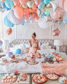 a woman sitting on top of a bed surrounded by balloons and desserts in front of her