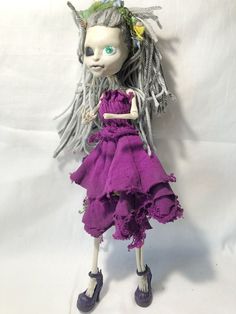 a doll with long hair and green eyes wearing a purple dress on a white background