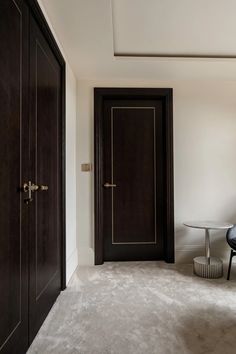 an empty room with two black doors and a glass table in the corner on one side