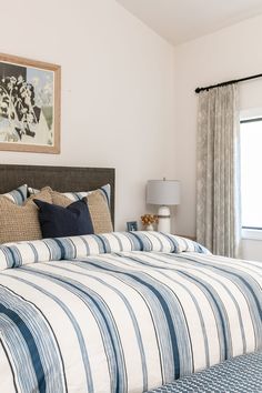 a bed with blue and white striped comforter next to a painting on the wall