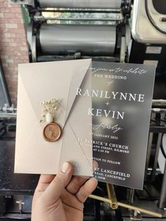 a person holding up a wedding card with a button on it