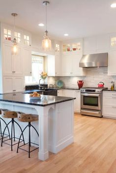 a large kitchen with white cabinets and black counter tops, an island in the middle is surrounded by bar stools