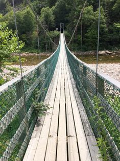 a wooden suspension bridge over a river surrounded by trees