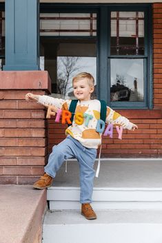 a young boy is sitting on the steps with his name spelled out in colorful letters