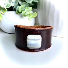 This handmade, brown leather cuff bracelet with white agate bead is made from high quality rawhide leather and features MishaGirl's signature design. It's a super cute leather accessory that goes well with a variety of styles. This also makes a great gift for women who love unique and interesting leather jewelry and accessories.  Fits wrist sizes 5 3/4 inches to 6 1/4 inches Inside Measurement 6 3/8 inches Width 1 1/2 inches at the widest part The leather cuff is dyed a dark brown color, which b Adjustable White Leather Bracelets, Brown Leather Rectangular Bracelet, Brown Rectangular Leather Jewelry, Brown Leather Rectangular Jewelry, Rectangular Leather Bracelet As A Gift, Rectangular Leather Bracelet For Gift, Rectangular Leather Bracelet Gift, Adjustable White Leather Bracelet, Brown Rectangular Leather Strap Bracelet