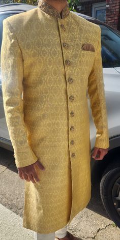 a man standing next to a white car wearing a yellow sherve coat and pants