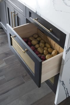 an open drawer in the middle of a kitchen counter with potatoes and apples inside it