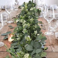 the table is set with white and green flowers, greenery, candles and wine glasses