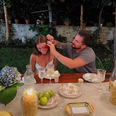 a man and woman are sitting at a table with plates, glasses and candles in front of them