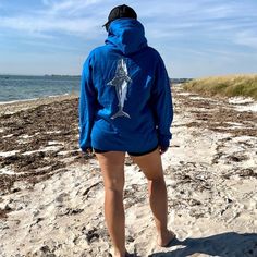 a person standing on the beach wearing a blue hoodie with a shark drawn on it