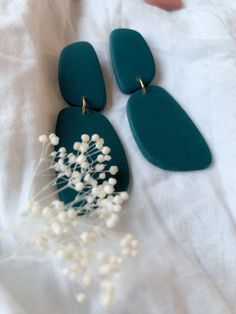 two green earrings with white flowers in front of them on a white cloth covered surface