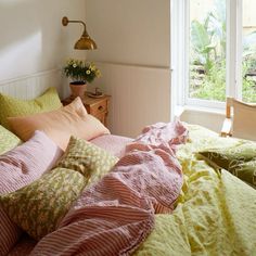 an unmade bed with pink and green sheets in a bedroom next to a window