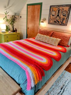 a bed with a colorful blanket on top of it in a bedroom next to a dresser