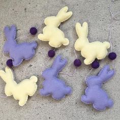 four felt bunny ornaments with purple and white balls hanging from strings on concrete surface, closeup