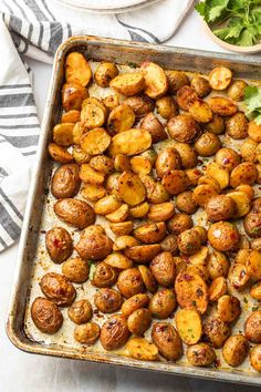 roasted potatoes on a baking sheet with parsley and cilantro in the background