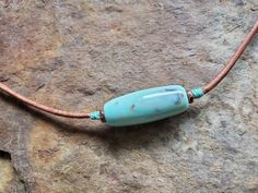 a blue beaded necklace sitting on top of a stone wall next to a brown cord