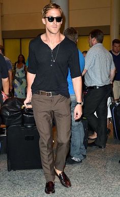 a man in black shirt and brown pants at an airport with his hand on his hip