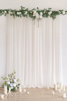 a table with candles, flowers and greenery on the top is set up in front of a white curtain