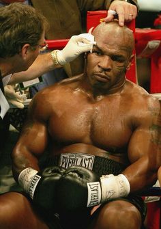 a man sitting in a boxing ring getting his hair cut by another man with gloves on