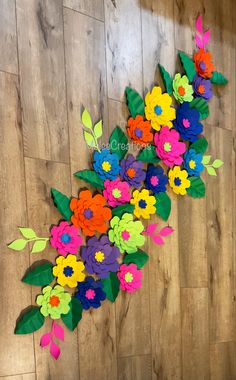 colorful paper flowers are arranged on a wood floor with green leaves and red, yellow, blue, pink, orange, and purple flowers