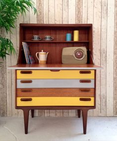 a yellow and grey dresser with some items on it's shelf next to a potted plant