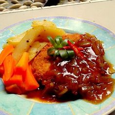 a blue and white plate topped with meat covered in gravy next to veggies