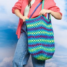 a woman holding a multicolored crocheted bag in front of a blue sky