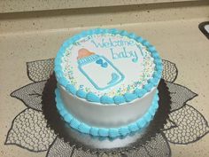 a blue and white baby shower cake on top of a doily with the words welcome baby