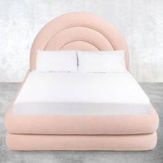 a bed with a pink headboard and white pillows on it's sides, in front of a concrete wall