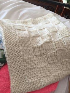 a white knitted blanket sitting on top of a bed next to a pink pillow