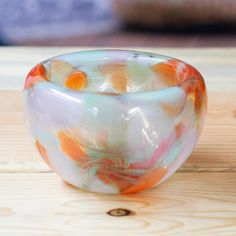 a colorful glass bowl sitting on top of a wooden table next to an orange and white object