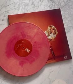 a pink vinyl record sitting on top of a white marble counter next to an album