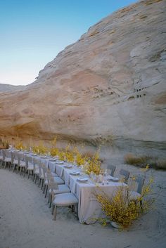 a long table set up in the desert with white linens and place settings on it