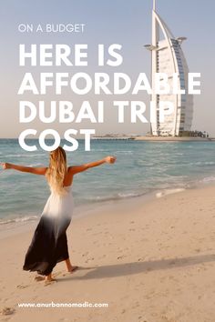 a woman standing on the beach with her arms spread out in front of the burj