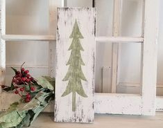 a wooden sign with a christmas tree painted on it next to a wreath and window